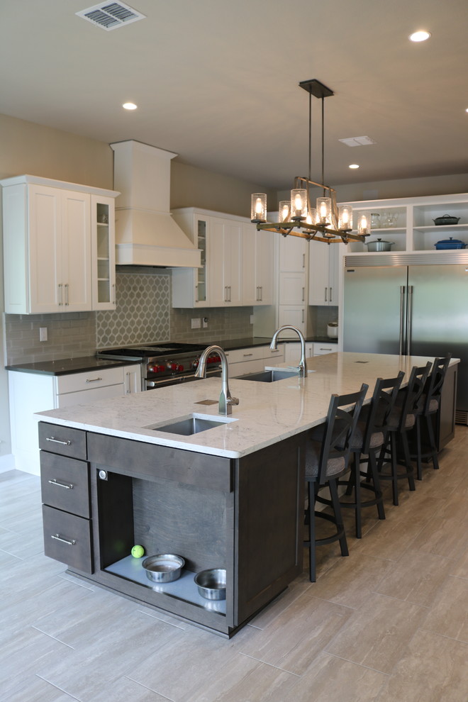 Transitional l-shaped porcelain tile and beige floor eat-in kitchen photo in Austin with a farmhouse sink, shaker cabinets, white cabinets, quartzite countertops, gray backsplash, glass tile backsplash, stainless steel appliances, two islands and black countertops