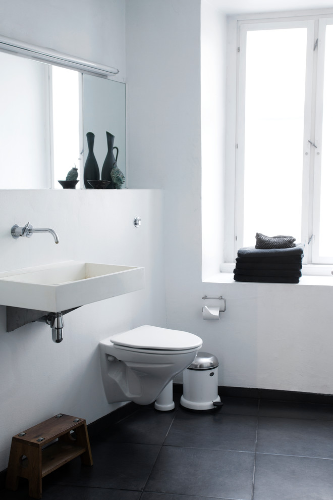 Design ideas for a mid-sized scandinavian master bathroom in Copenhagen with a wall-mount toilet, white walls, ceramic floors and a trough sink.