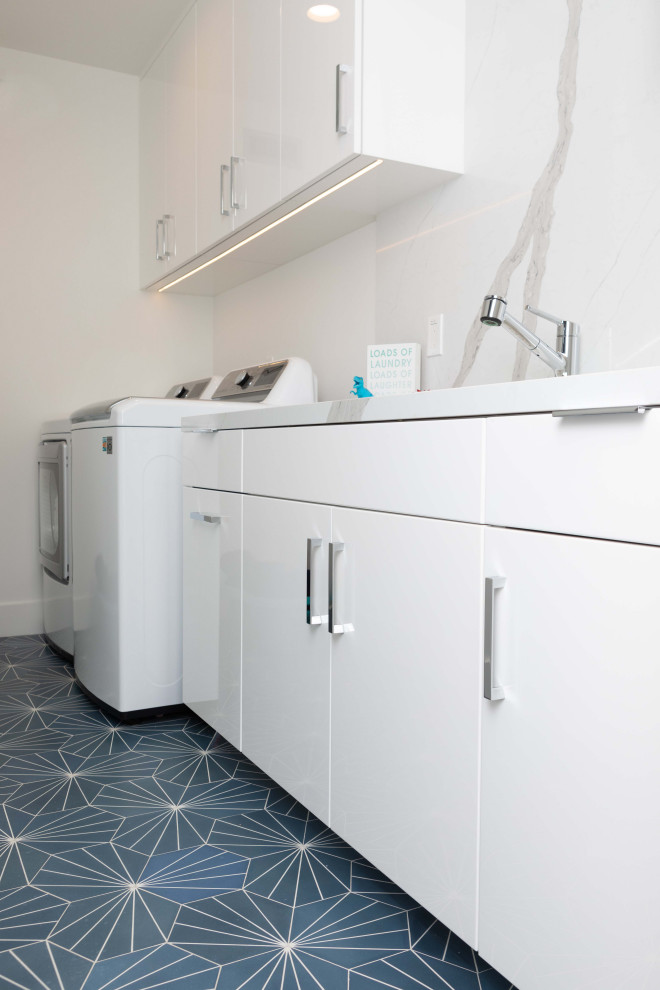 This is an example of a large contemporary galley dedicated laundry room in Orange County with an undermount sink, flat-panel cabinets, white cabinets, quartz benchtops, white walls, concrete floors, a side-by-side washer and dryer, blue floor and white benchtop.
