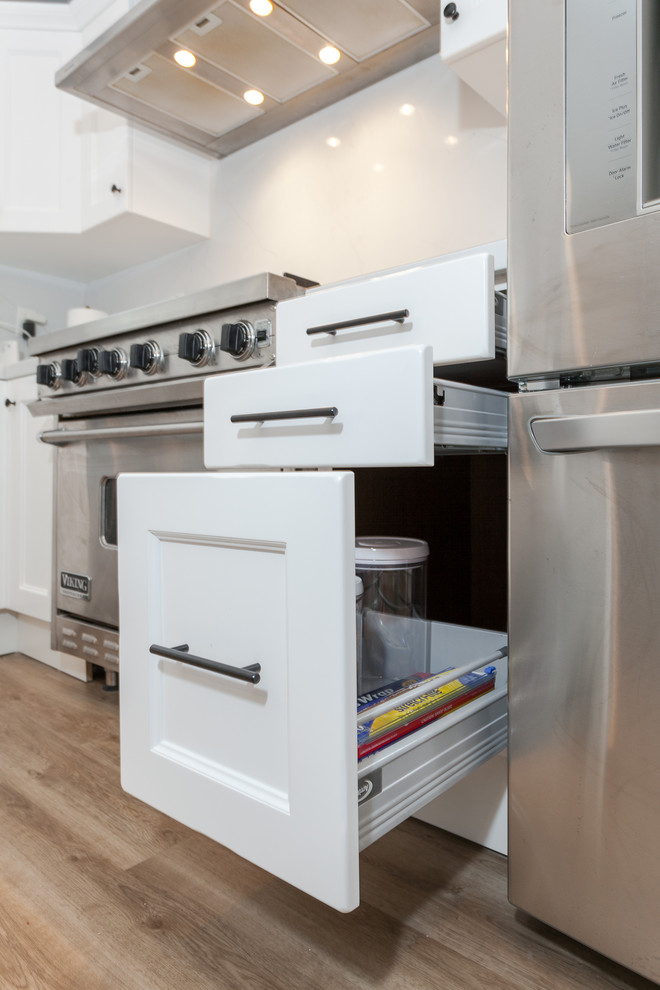 Mid-sized modern l-shaped eat-in kitchen in Los Angeles with an undermount sink, beaded inset cabinets, white cabinets, quartz benchtops, white splashback, porcelain splashback, stainless steel appliances, vinyl floors, with island, brown floor and white benchtop.