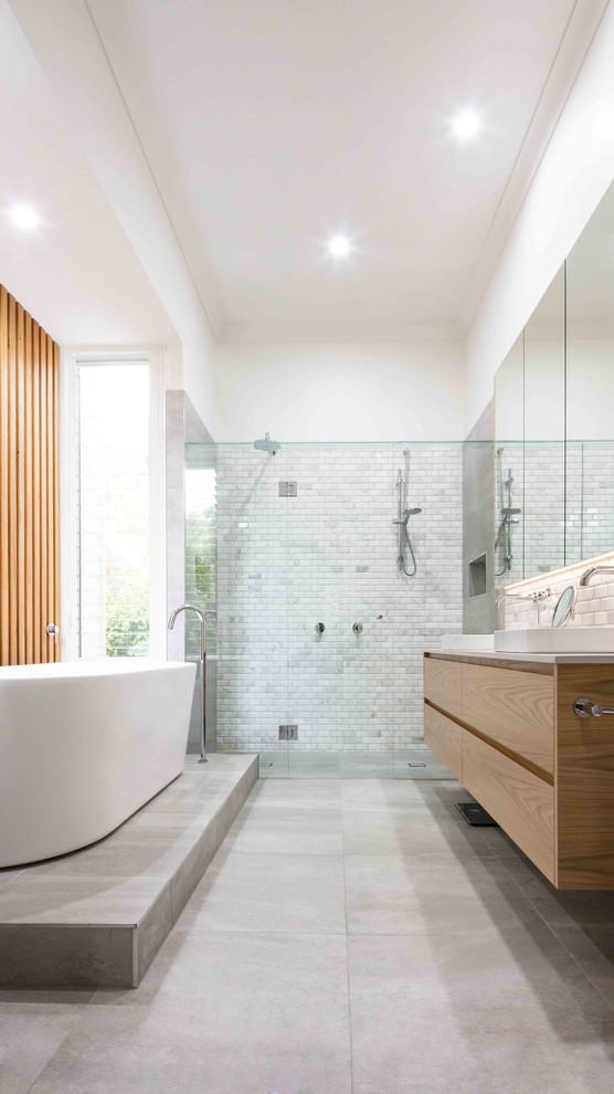 This is an example of a contemporary master bathroom in Melbourne with light wood cabinets, marble, white walls, cement tiles, engineered quartz benchtops, grey floor, flat-panel cabinets, a freestanding tub, a curbless shower, gray tile, a vessel sink, a hinged shower door and white benchtops.