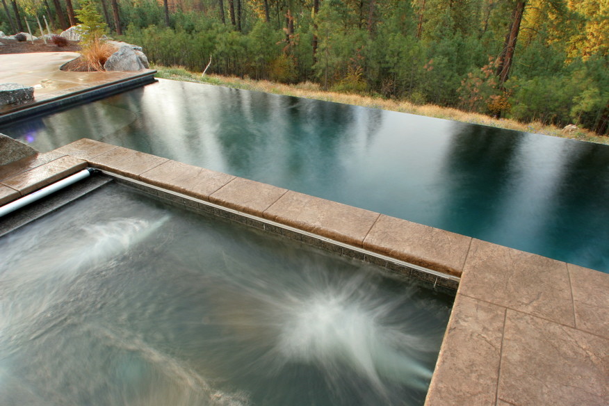 Design ideas for a mid-sized contemporary backyard rectangular infinity pool in Seattle with a hot tub and stamped concrete.
