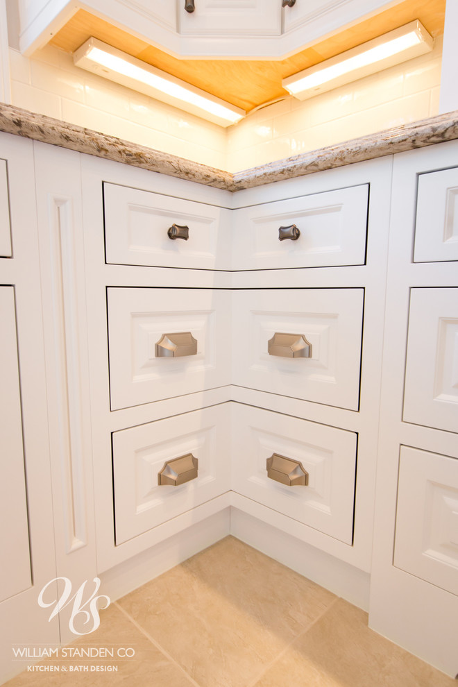 Inspiration for a mid-sized transitional u-shaped porcelain tile eat-in kitchen remodel in Toronto with an undermount sink, raised-panel cabinets, white cabinets, quartzite countertops, beige backsplash, stone slab backsplash, stainless steel appliances and an island