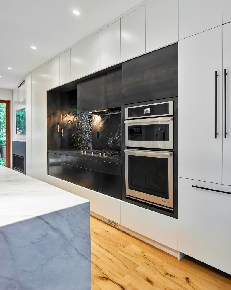 Mid-sized contemporary galley eat-in kitchen in Toronto with flat-panel cabinets, white cabinets, marble benchtops, black splashback, slate splashback, stainless steel appliances, medium hardwood floors, with island and white benchtop.