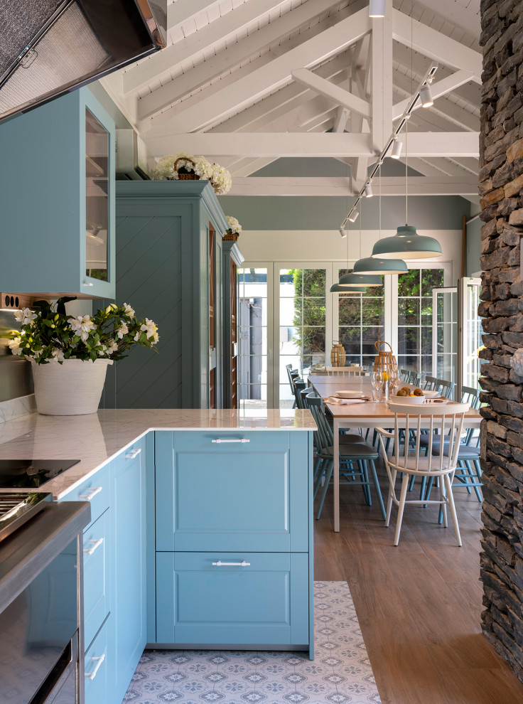 Inspiration for an expansive transitional l-shaped eat-in kitchen in Bilbao with an undermount sink, glass-front cabinets, blue cabinets, quartz benchtops, metallic splashback, metal splashback, stainless steel appliances, terra-cotta floors, a peninsula, blue floor and white benchtop.