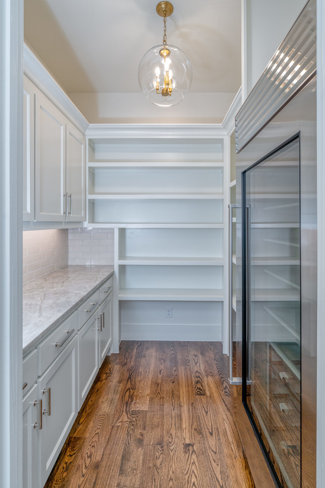 Mid-sized transitional u-shaped kitchen pantry in Dallas with a farmhouse sink, recessed-panel cabinets, white cabinets, limestone benchtops, beige splashback, ceramic splashback, stainless steel appliances, dark hardwood floors, with island, brown floor and grey benchtop.