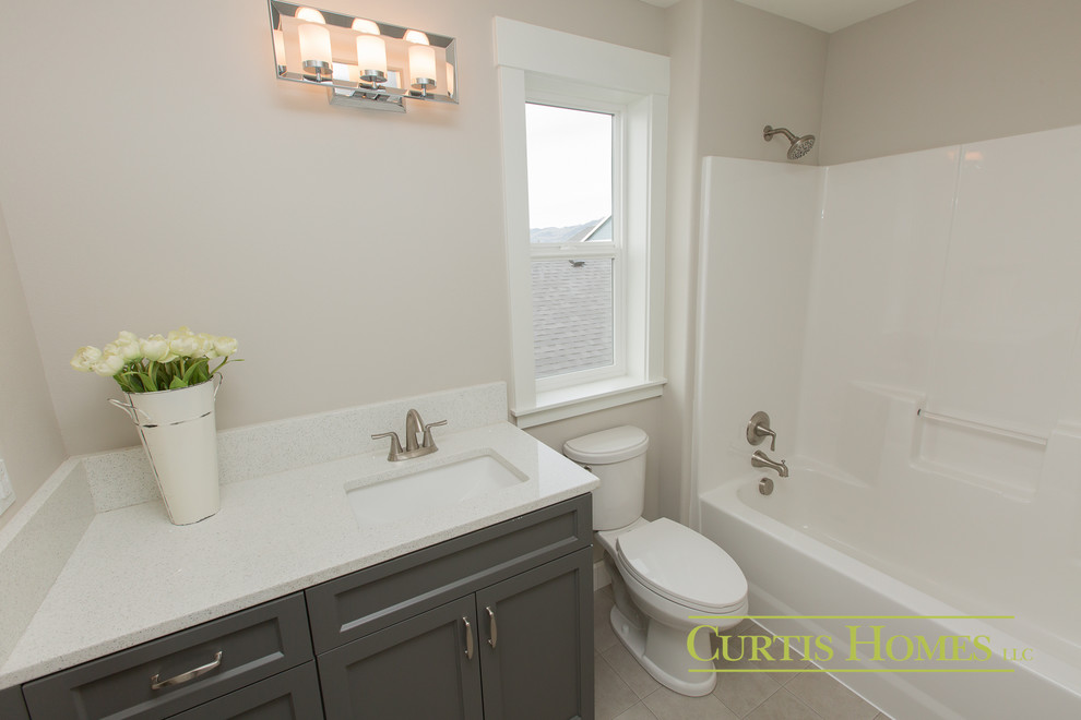 This is an example of a small country kids bathroom in Portland with flat-panel cabinets, grey cabinets, a shower/bathtub combo, a one-piece toilet, white tile, grey walls, a drop-in sink and granite benchtops.