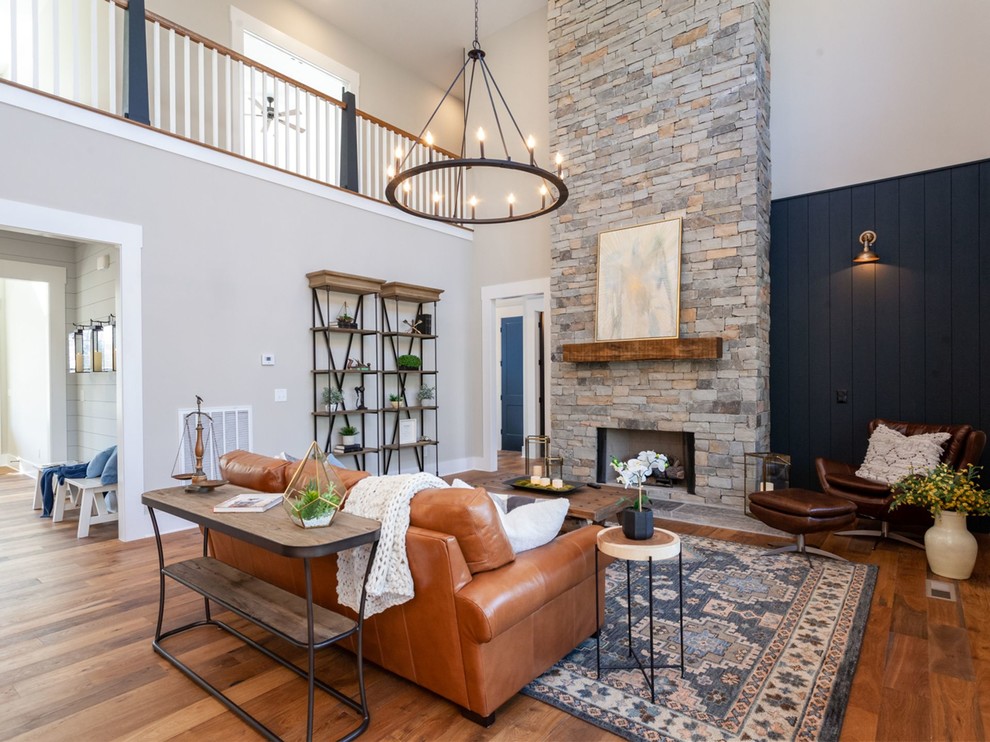 Photo of a mid-sized country formal open concept living room in Other with grey walls, medium hardwood floors, a standard fireplace, a stone fireplace surround, no tv and brown floor.