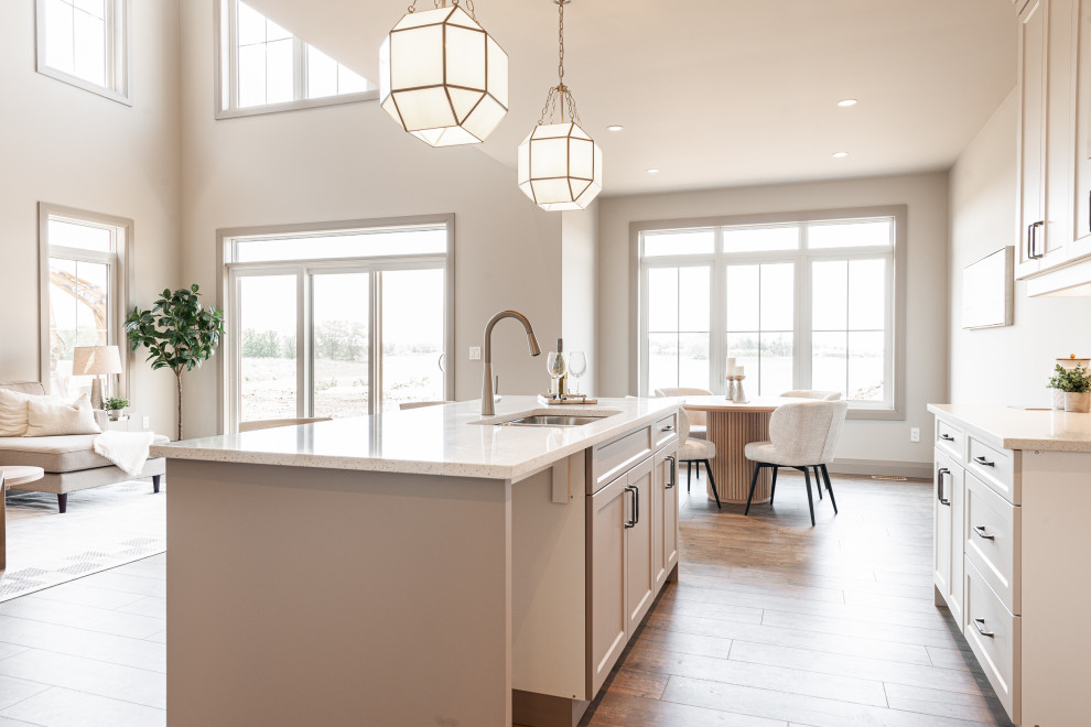 Small transitional galley laminate floor and brown floor open concept kitchen photo in Toronto with a double-bowl sink, recessed-panel cabinets, beige cabinets, quartz countertops, beige backsplash, porcelain backsplash, stainless steel appliances, an island and white countertops