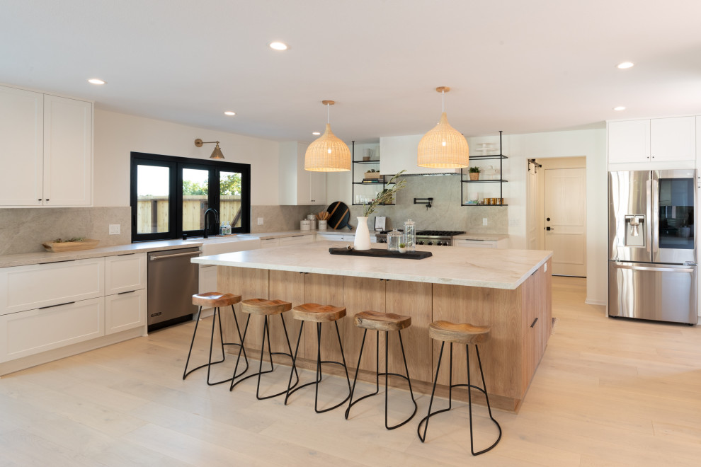 This is an example of a large modern u-shaped open plan kitchen in Santa Barbara with a farmhouse sink, flat-panel cabinets, light wood cabinets, quartzite benchtops, white splashback, stone slab splashback, stainless steel appliances, light hardwood floors, with island and white benchtop.