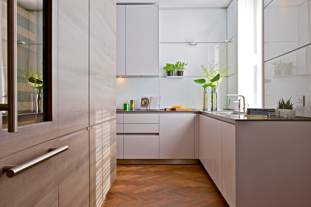 Design ideas for a large contemporary l-shaped separate kitchen in London with an undermount sink, flat-panel cabinets, light wood cabinets, white splashback, medium hardwood floors, no island, glass benchtops, glass tile splashback and panelled appliances.