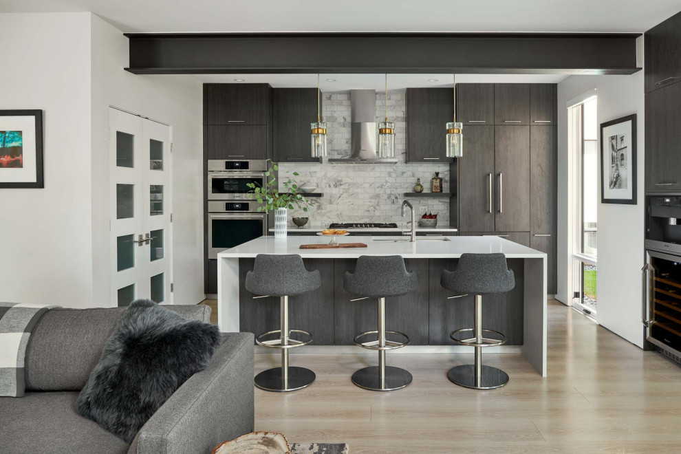 Photo of a mid-sized contemporary u-shaped eat-in kitchen in Denver with an undermount sink, flat-panel cabinets, dark wood cabinets, quartz benchtops, white splashback, marble splashback, stainless steel appliances, light hardwood floors, with island, beige floor, white benchtop and exposed beam.