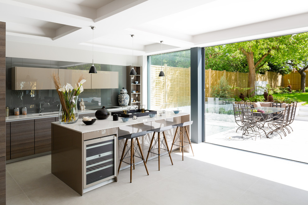 Inspiration for a contemporary galley open plan kitchen in London with flat-panel cabinets, beige cabinets, grey splashback, glass sheet splashback, with island and beige floor.