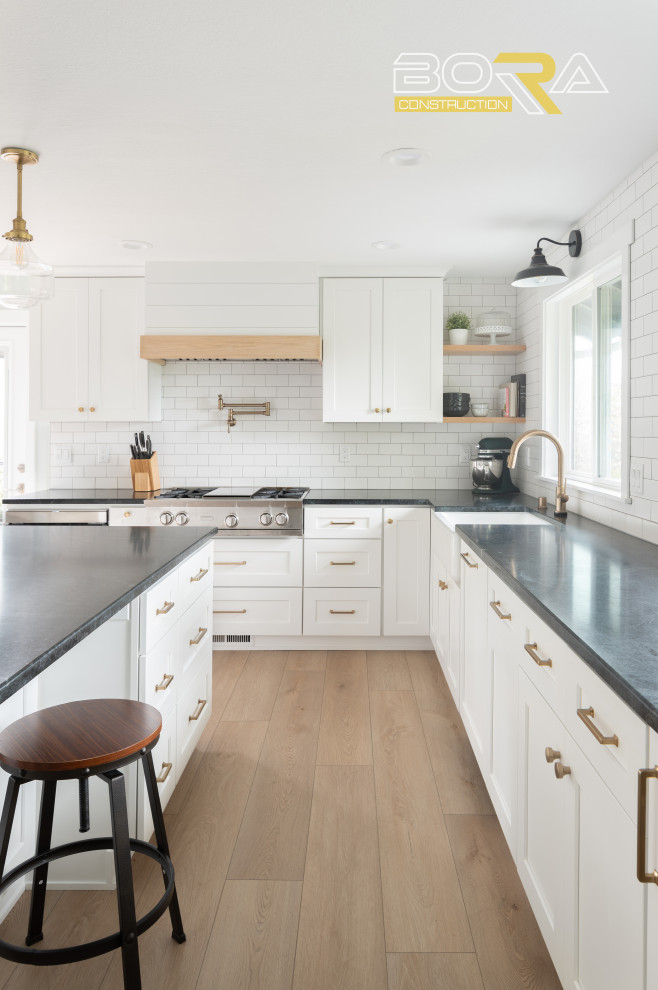 Example of a mid-sized transitional u-shaped medium tone wood floor and brown floor eat-in kitchen design in Seattle with shaker cabinets, white cabinets, quartz countertops, white backsplash, ceramic backsplash, stainless steel appliances, an island and black countertops
