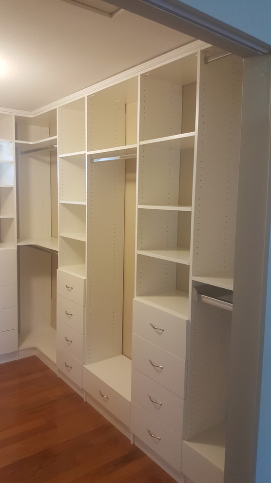 Large modern gender-neutral walk-in wardrobe in Vancouver with white cabinets, laminate floors and brown floor.
