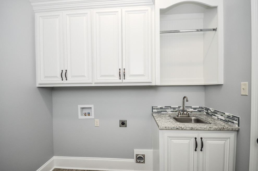 Design ideas for a mid-sized traditional galley dedicated laundry room in New Orleans with a drop-in sink, raised-panel cabinets, white cabinets, granite benchtops, grey walls, ceramic floors and a side-by-side washer and dryer.