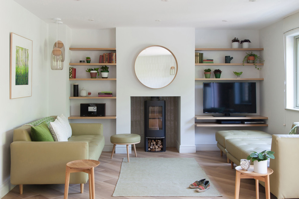 This is an example of a scandinavian formal enclosed living room in Cambridgeshire with light hardwood floors, a wood stove, a freestanding tv and beige floor.