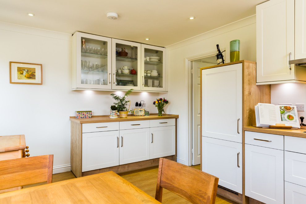 Design ideas for a small traditional l-shaped eat-in kitchen in Hampshire with a single-bowl sink, shaker cabinets, white cabinets, laminate benchtops, green splashback, glass sheet splashback, stainless steel appliances and light hardwood floors.