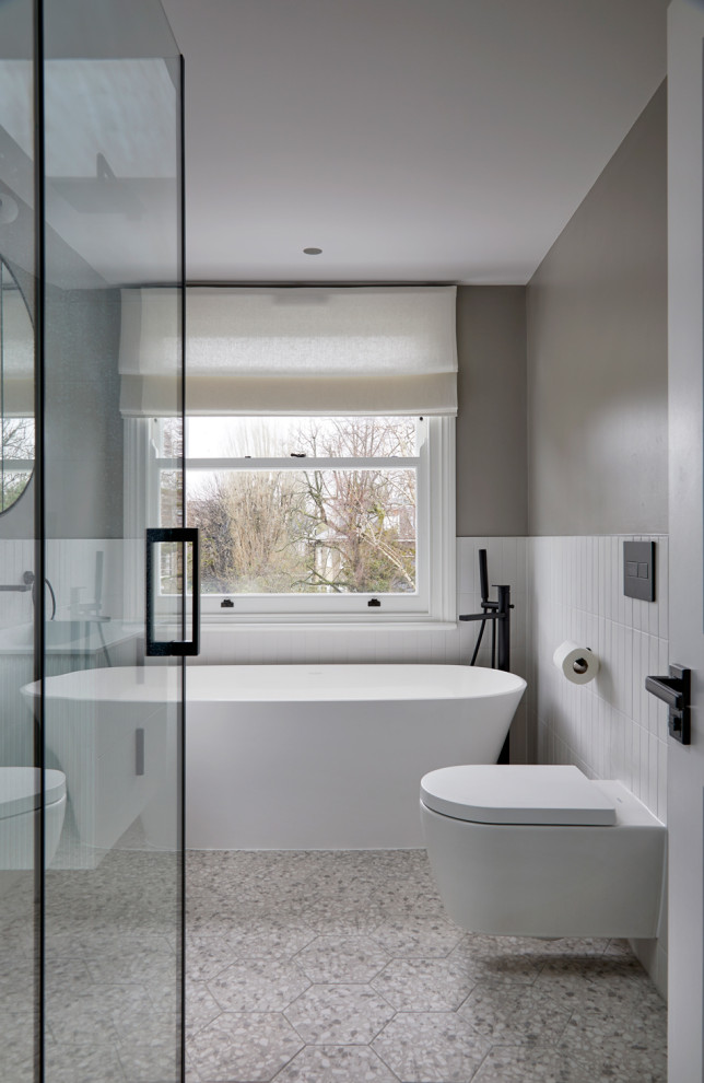 Свежая идея для дизайна: детская ванная комната среднего размера в современном стиле с плоскими фасадами, белыми фасадами, отдельно стоящей ванной, угловым душем, инсталляцией, белой плиткой, керамической плиткой, серыми стенами, полом из керамической плитки, подвесной раковиной, столешницей из гранита, разноцветным полом, душем с распашными дверями, белой столешницей, тумбой под одну раковину и подвесной тумбой - отличное фото интерьера