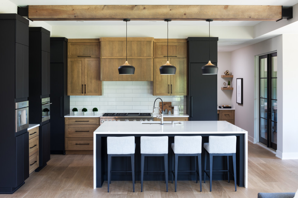 This is an example of a transitional l-shaped eat-in kitchen in Minneapolis with a single-bowl sink, flat-panel cabinets, black cabinets, quartz benchtops, white splashback, porcelain splashback, black appliances, with island, white benchtop, medium hardwood floors and brown floor.