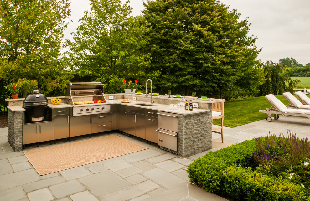 This is an example of a large traditional backyard patio in New York with an outdoor kitchen, an awning and concrete pavers.
