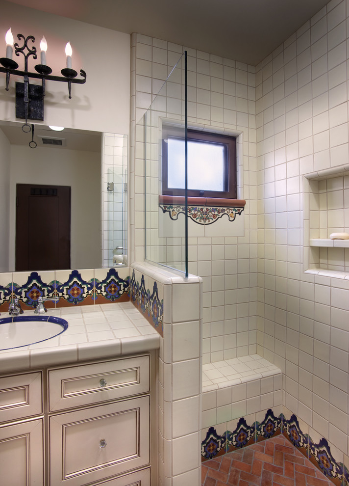 Design ideas for a mediterranean bathroom in San Diego with an undermount sink, raised-panel cabinets, white cabinets, tile benchtops, an open shower, multi-coloured tile, terra-cotta tile, white walls and terra-cotta floors.