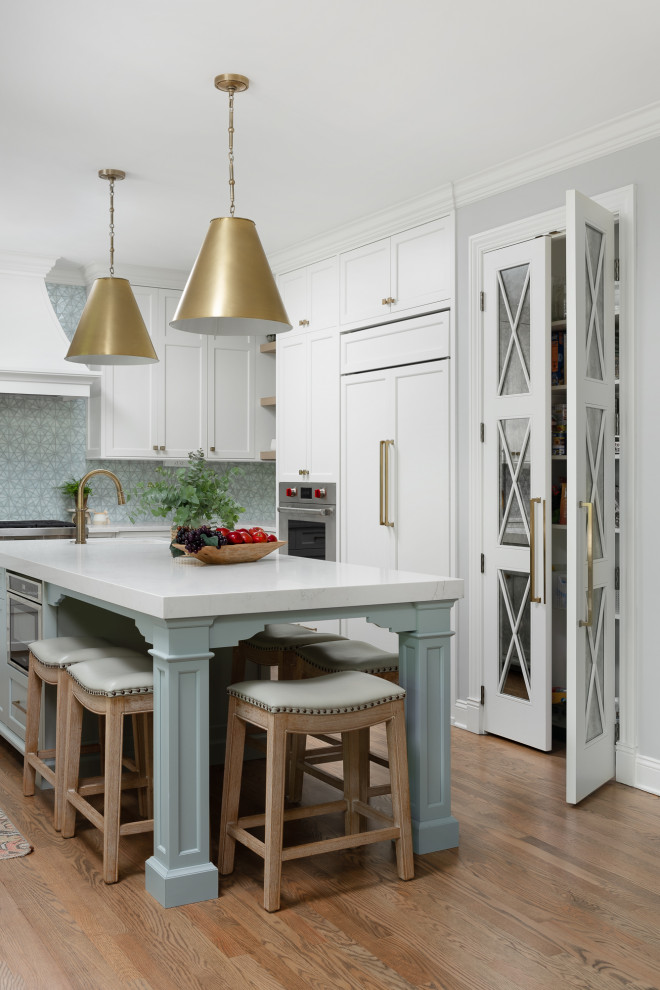 Example of a large beach style u-shaped medium tone wood floor and brown floor kitchen pantry design in Chicago with a farmhouse sink, shaker cabinets, white cabinets, quartz countertops, blue backsplash, glass tile backsplash, paneled appliances, an island and white countertops