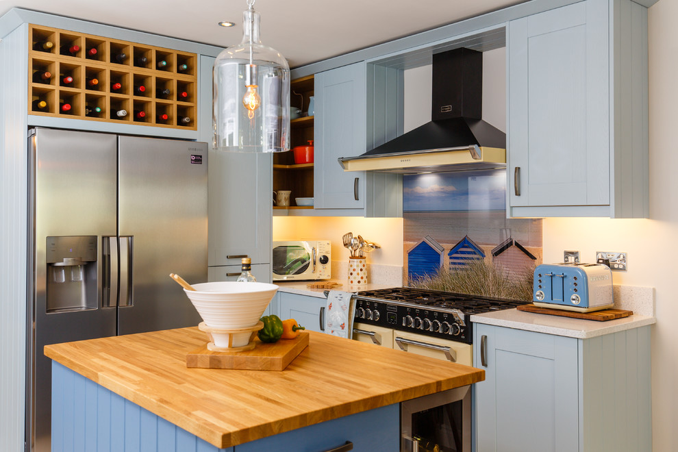 Photo of a beach style u-shaped open plan kitchen in Cambridgeshire with shaker cabinets, wood benchtops, glass sheet splashback, panelled appliances, with island, a farmhouse sink, light hardwood floors and grey cabinets.