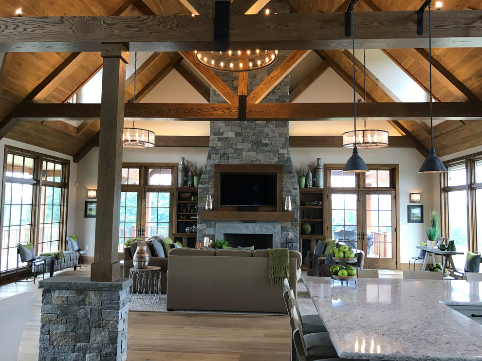 Inspiration for a large country loft-style living room in Philadelphia with beige walls, medium hardwood floors, a standard fireplace, a stone fireplace surround, a wall-mounted tv and brown floor.