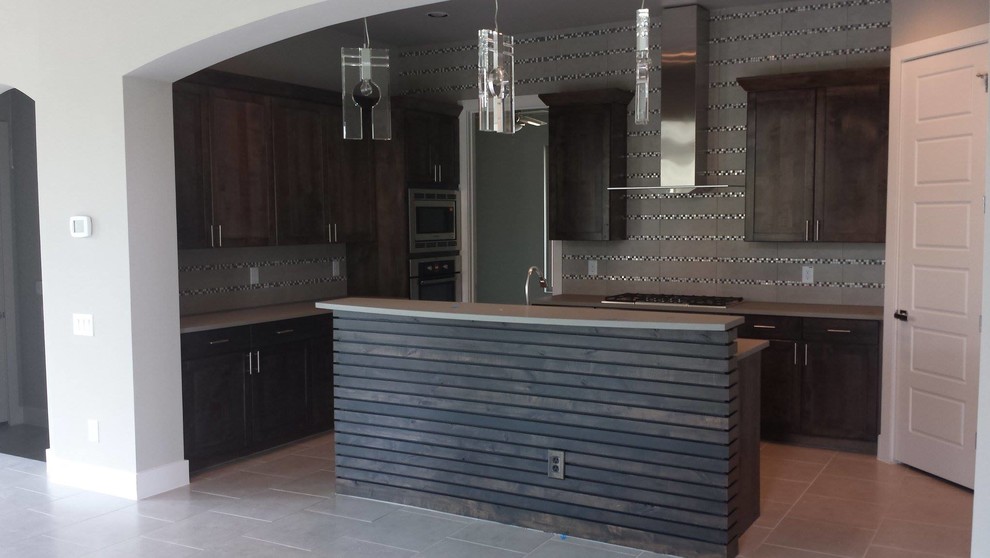 L-shaped eat-in kitchen in Austin with recessed-panel cabinets, dark wood cabinets, solid surface benchtops, grey splashback, glass tile splashback, stainless steel appliances, linoleum floors and with island.
