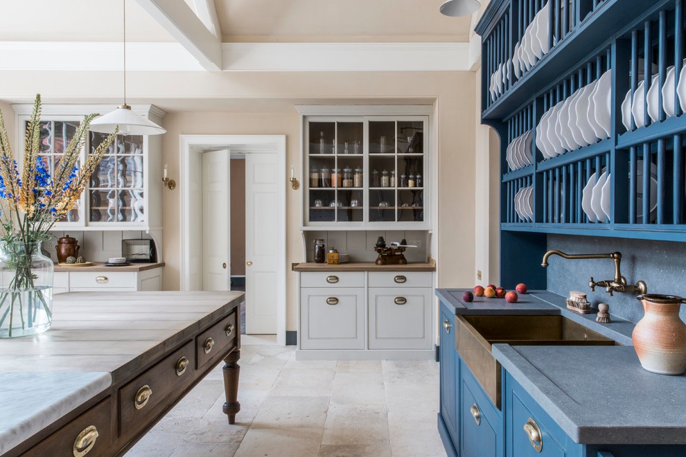 Large traditional l-shaped kitchen in Hampshire with a farmhouse sink, distressed cabinets, marble benchtops, white splashback, porcelain splashback, black appliances, limestone floors, with island, beige floor and white benchtop.