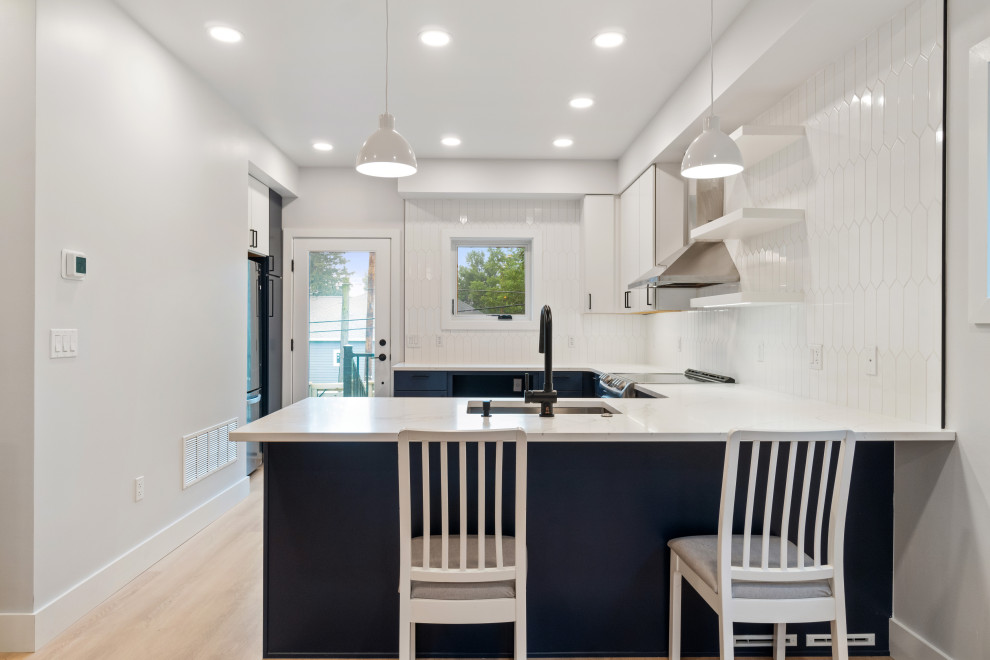 Kitchen - small modern u-shaped laminate floor and beige floor kitchen idea with an undermount sink, flat-panel cabinets, white cabinets, white backsplash, ceramic backsplash, stainless steel appliances and a peninsula