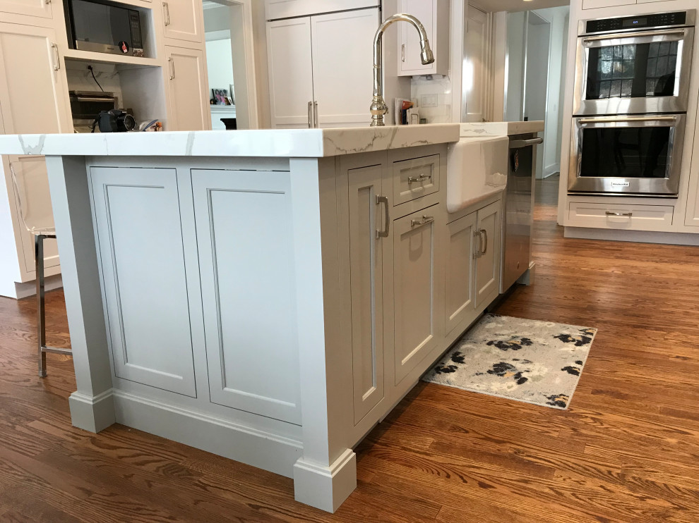 Inspiration for a large transitional u-shaped medium tone wood floor and brown floor eat-in kitchen remodel with a farmhouse sink, recessed-panel cabinets, white cabinets, quartz countertops, white backsplash, subway tile backsplash, stainless steel appliances, an island and white countertops