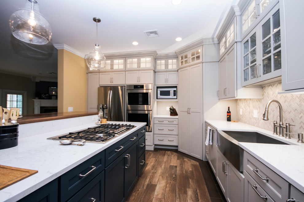 Large traditional l-shaped kitchen in Providence with a farmhouse sink, recessed-panel cabinets, white cabinets, quartz benchtops, multi-coloured splashback, limestone splashback, stainless steel appliances, dark hardwood floors, with island, brown floor and white benchtop.