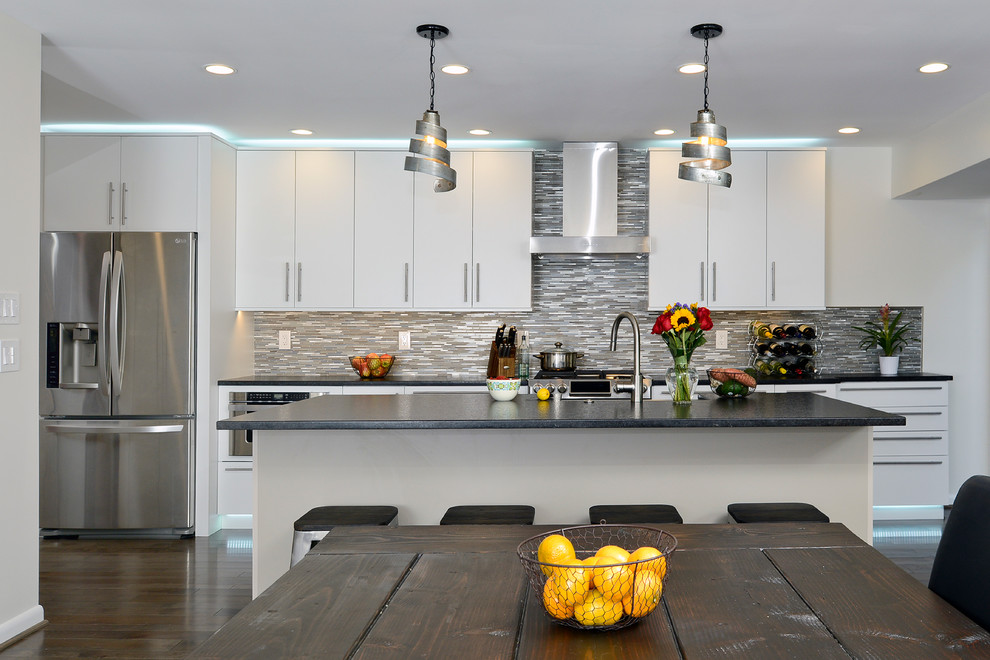 Photo of a mid-sized modern single-wall eat-in kitchen in DC Metro with a farmhouse sink, flat-panel cabinets, white cabinets, granite benchtops, brown splashback, mosaic tile splashback, stainless steel appliances, dark hardwood floors and with island.