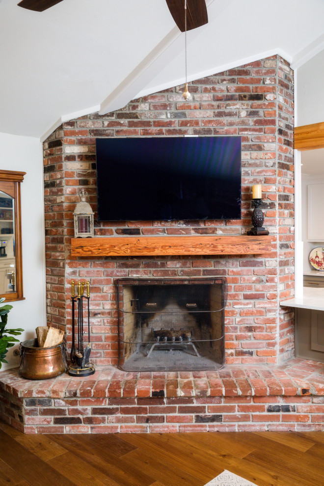 ニューオリンズにある中くらいなトラディショナルスタイルのおしゃれなLDK (グレーの壁、無垢フローリング、コーナー設置型暖炉、レンガの暖炉まわり、壁掛け型テレビ、茶色い床、三角天井) の写真