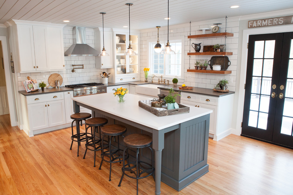 Eat-in kitchen - mid-sized transitional u-shaped medium tone wood floor eat-in kitchen idea in Chicago with a farmhouse sink, recessed-panel cabinets, white cabinets, quartz countertops, multicolored backsplash, subway tile backsplash, stainless steel appliances and an island