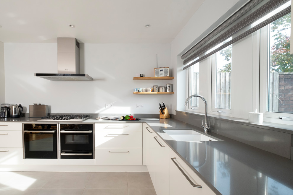 This is an example of a small contemporary l-shaped kitchen in Cardiff with flat-panel cabinets, white cabinets, quartzite benchtops, porcelain floors, grey floor, grey benchtop, an undermount sink, black appliances and grey splashback.