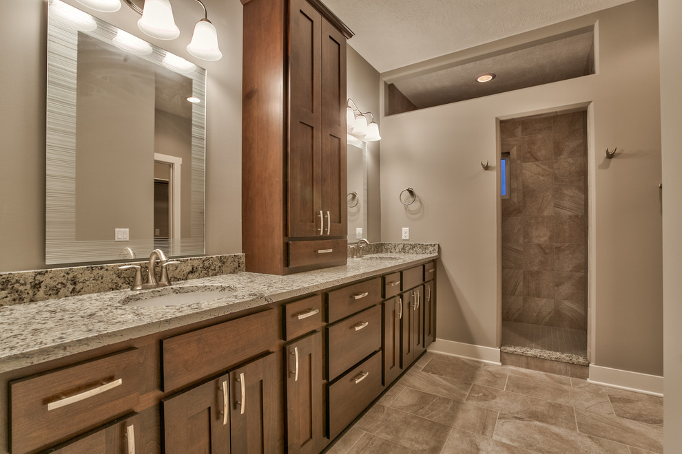 This is an example of a mid-sized mediterranean master bathroom in Omaha with an undermount sink, recessed-panel cabinets, medium wood cabinets, granite benchtops, an open shower, gray tile, ceramic tile, grey walls and ceramic floors.
