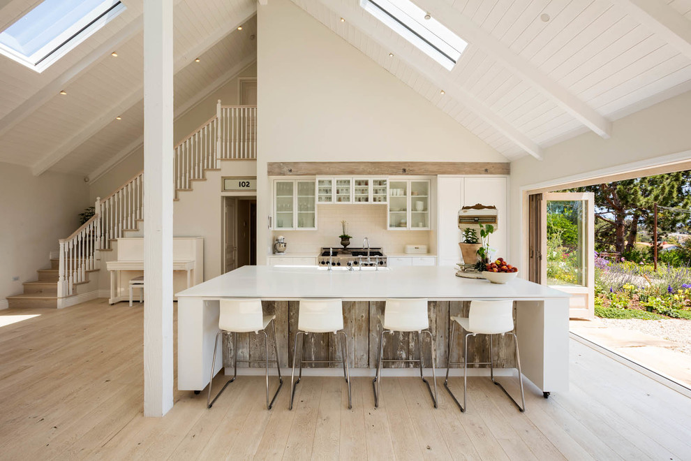 Inspiration for a country galley open plan kitchen in Los Angeles with a farmhouse sink, glass-front cabinets, white cabinets, stainless steel appliances, light hardwood floors and with island.