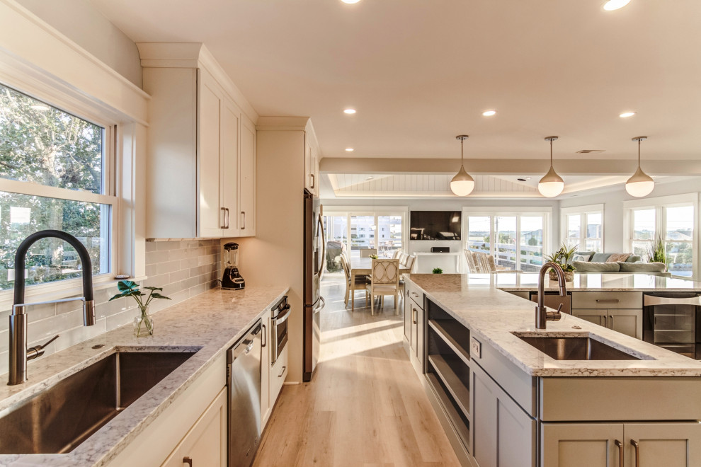 Inspiration for a large beach style l-shaped open plan kitchen in Wilmington with an undermount sink, shaker cabinets, grey cabinets, quartz benchtops, grey splashback, porcelain splashback, stainless steel appliances, laminate floors, with island, multi-coloured floor and white benchtop.