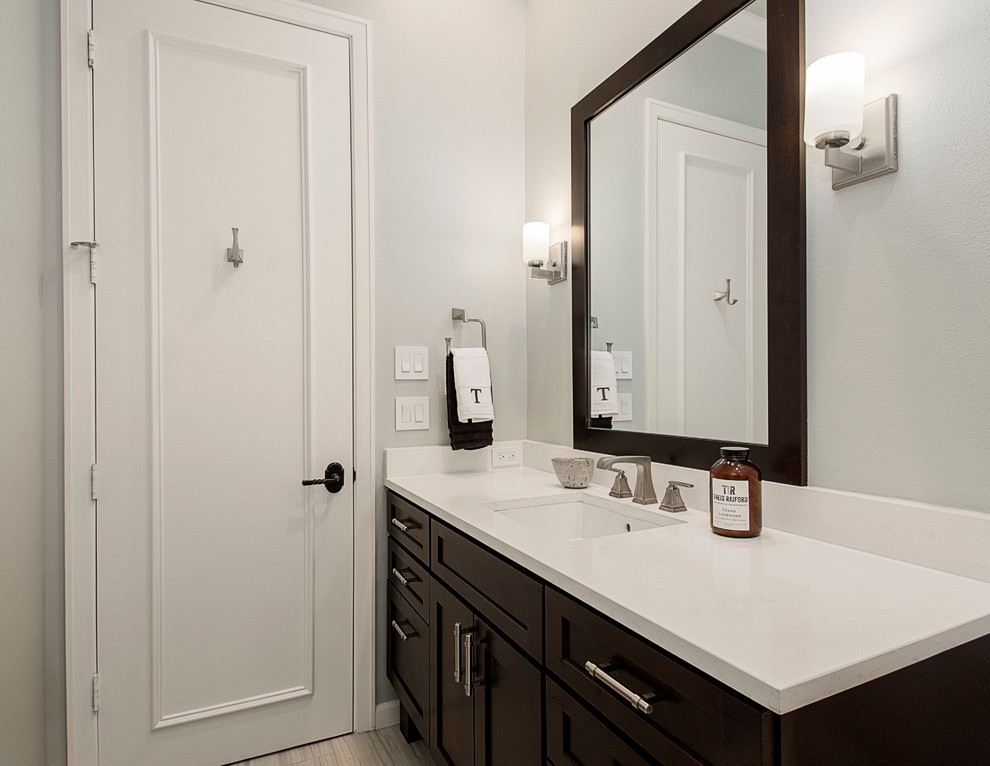 Photo of a mid-sized transitional 3/4 bathroom in Dallas with shaker cabinets, dark wood cabinets, a shower/bathtub combo, a one-piece toilet, black and white tile, ceramic tile, grey walls, porcelain floors, an undermount sink and solid surface benchtops.