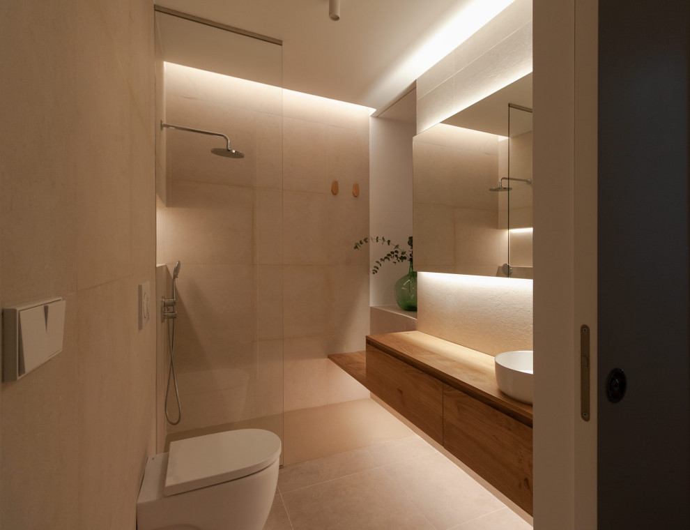 This is an example of a contemporary ensuite bathroom in Barcelona with freestanding cabinets, medium wood cabinets, a walk-in shower, an urinal, beige tiles, ceramic tiles, beige walls, ceramic flooring, a vessel sink, wooden worktops, beige floors, an open shower, brown worktops, an enclosed toilet, a single sink and a floating vanity unit.