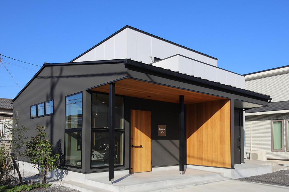 Aménagement d'une façade de maison noire moderne en stuc et planches et couvre-joints à un étage avec un toit à deux pans, un toit en métal et un toit bleu.