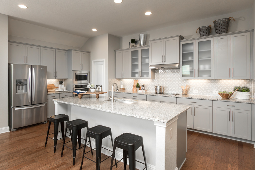 Transitional u-shaped medium tone wood floor and brown floor kitchen photo with an undermount sink, shaker cabinets, gray cabinets, gray backsplash, stainless steel appliances, an island and gray countertops