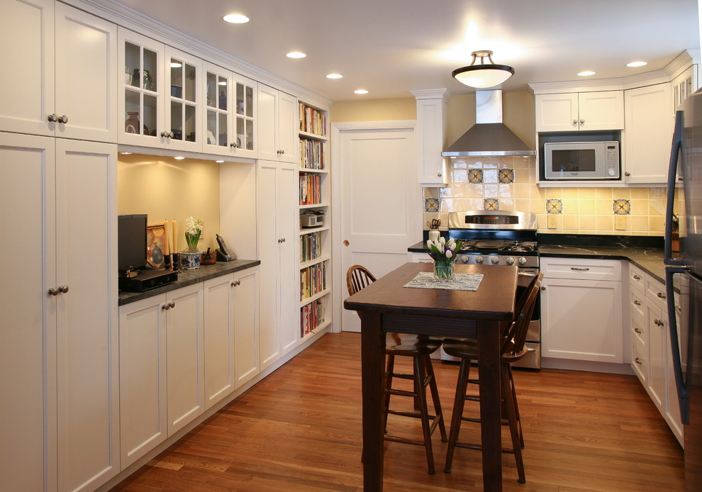 This is an example of a mid-sized traditional l-shaped separate kitchen in Boston with a single-bowl sink, shaker cabinets, white cabinets, soapstone benchtops, stainless steel appliances, medium hardwood floors, yellow splashback, porcelain splashback, with island and brown floor.