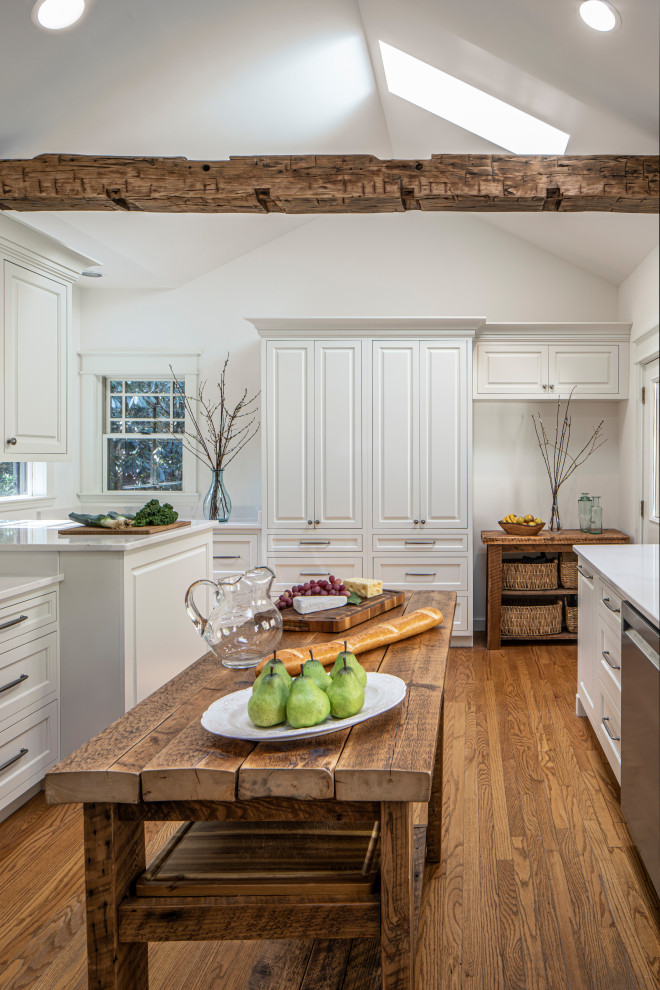 This is an example of a mid-sized transitional l-shaped kitchen pantry in Charlotte with an undermount sink, raised-panel cabinets, white cabinets, quartz benchtops, white splashback, engineered quartz splashback, stainless steel appliances, dark hardwood floors, brown floor, white benchtop and exposed beam.