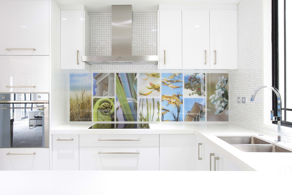 Design ideas for a mid-sized contemporary l-shaped kitchen in Auckland with solid surface benchtops, blue splashback, glass sheet splashback, stainless steel appliances and with island.