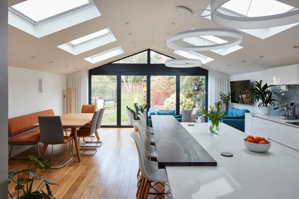 Photo of a large modern galley kitchen/diner in London with a built-in sink, flat-panel cabinets, white cabinets, granite worktops, grey splashback, metal splashback, integrated appliances, dark hardwood flooring, an island, brown floors and white worktops.
