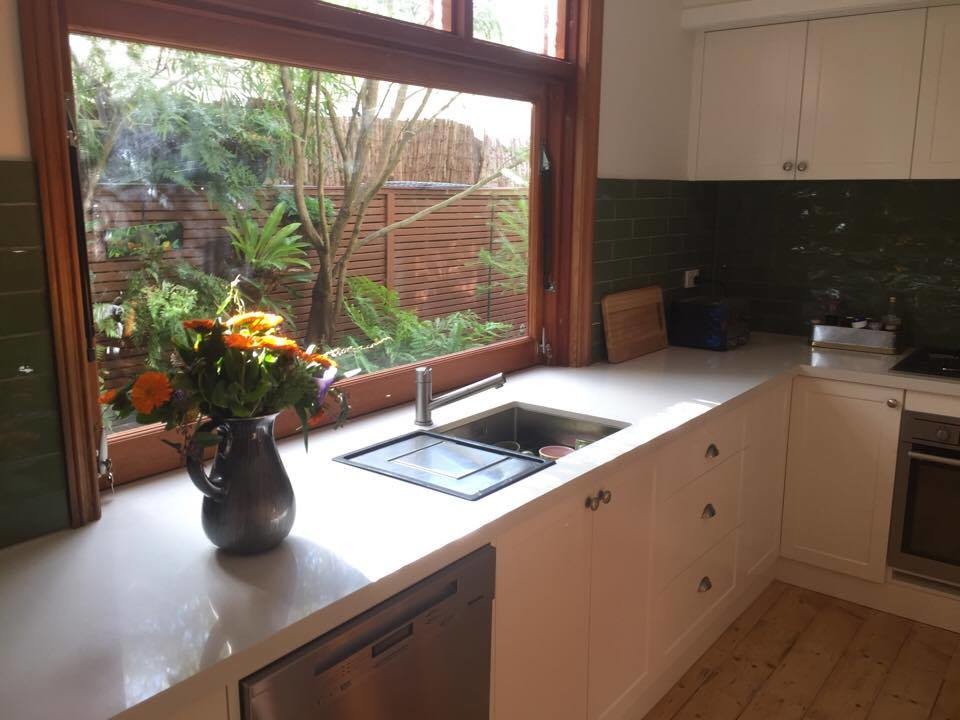 Design ideas for a mid-sized country u-shaped eat-in kitchen in Melbourne with a single-bowl sink, shaker cabinets, white cabinets, granite benchtops, green splashback, ceramic splashback, stainless steel appliances, light hardwood floors and white benchtop.